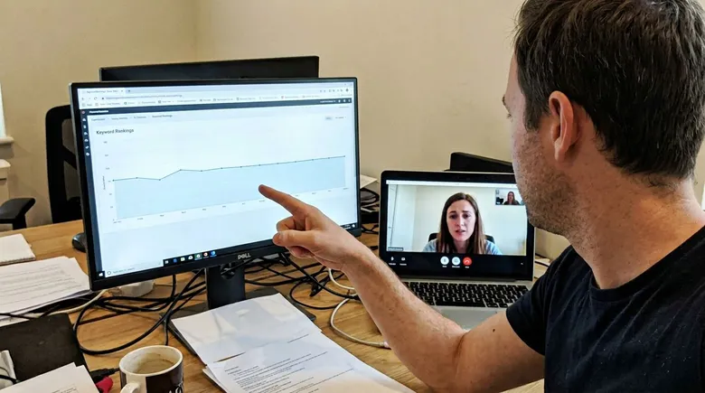 SCENE: Agency owner pointing at a ranking graph on a monitor showing flat movement while client watches on video call